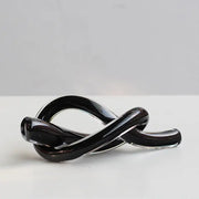 A sleek glossy black geometric glass sculpture with a smooth intertwined knot design for modern decorbites decor