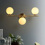 Brass-finished modern wall light with three white glass shades for bedroom featuring frosted glass globes