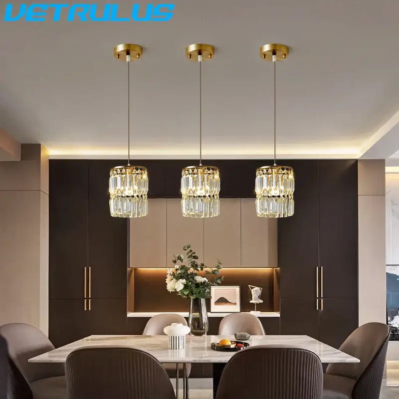Three elegant gold-finished crystal chandelier pendant lights with faceted glass hang above a modern dining table