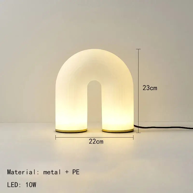 A sleek u-shaped table lamp with a white acrylic body and gold metal base complementing modern pendant lights design