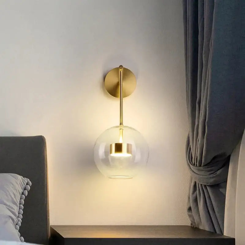Modern gold wall lamp with adjustable direction featuring a spherical glass shade for minimalist bedroom lighting decorbites