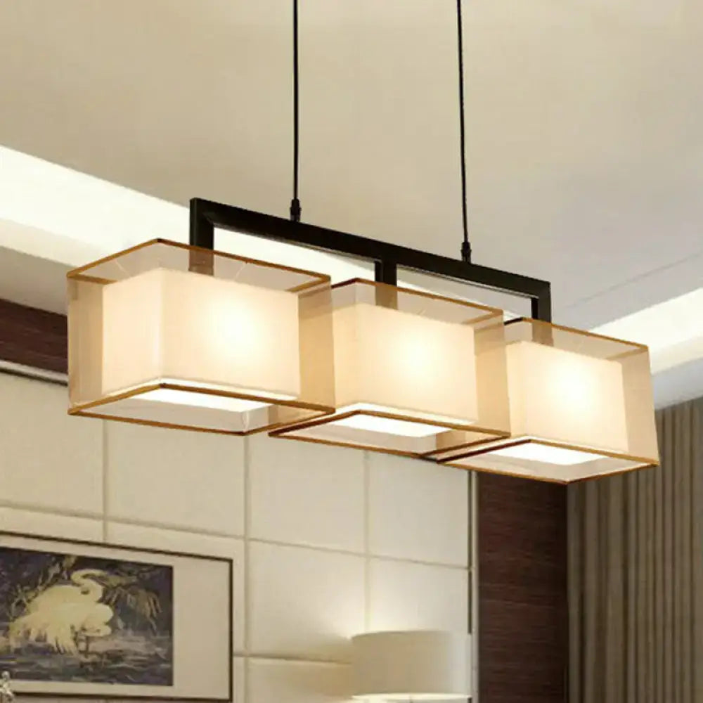 Modern gold and beige fabric island light with three illuminated shades and black suspension lighting bar for kitchen use
