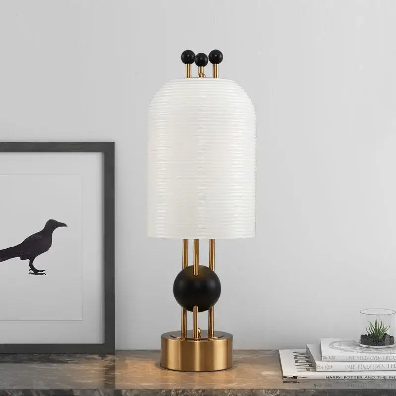 Modern table lamp with white ribbed paper shade, gold-toned metal base, and black details complements glass led chandelier decor