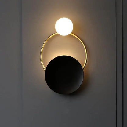 Modern gold and black orb wall lamp with a glowing white spherical bulb above a gold ring and matte black disc for living rooms