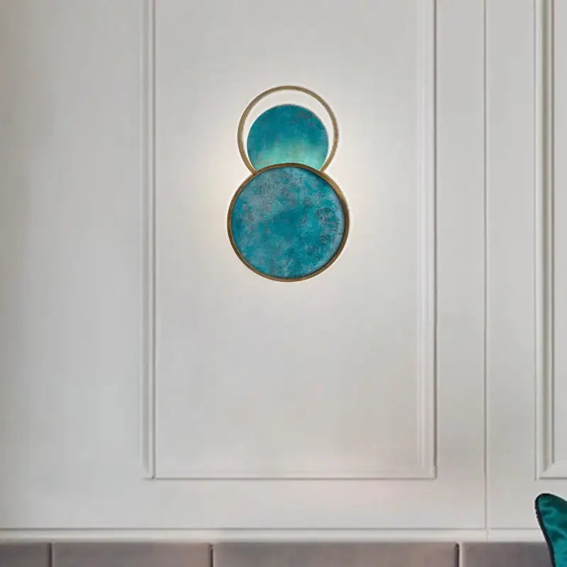 Modern teal circular wall lamp with brushed gold frame and textured glass panels for elegant living room decor