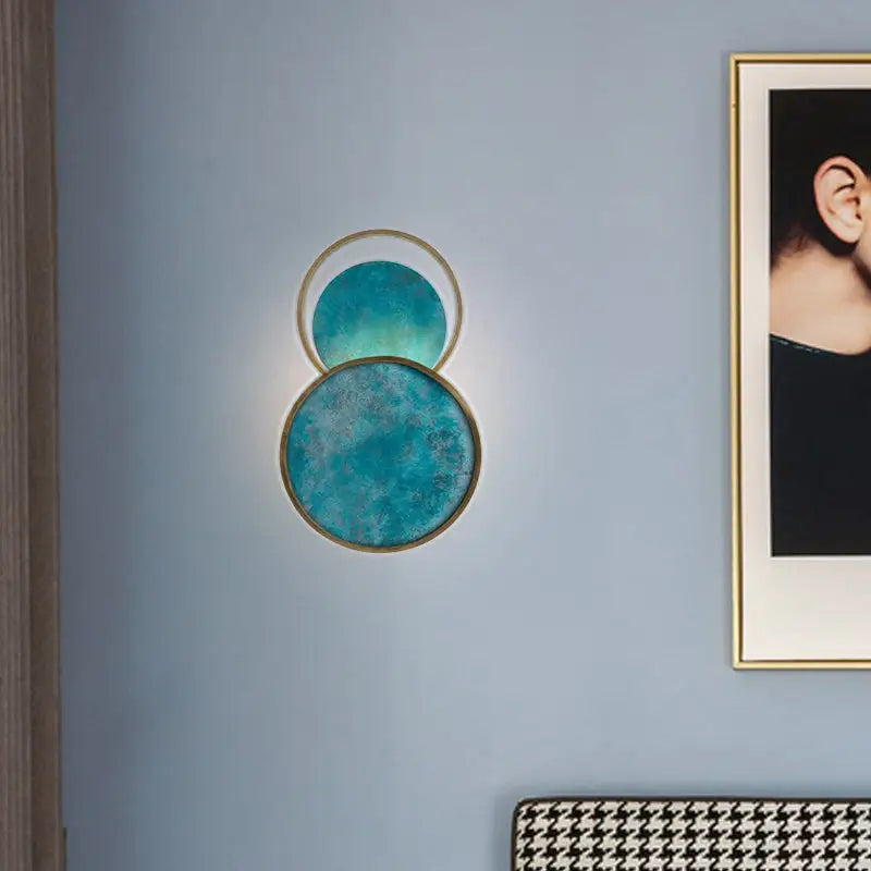 Modern teal circular wall sconce with gold-toned frames and a textured, gradient finish.