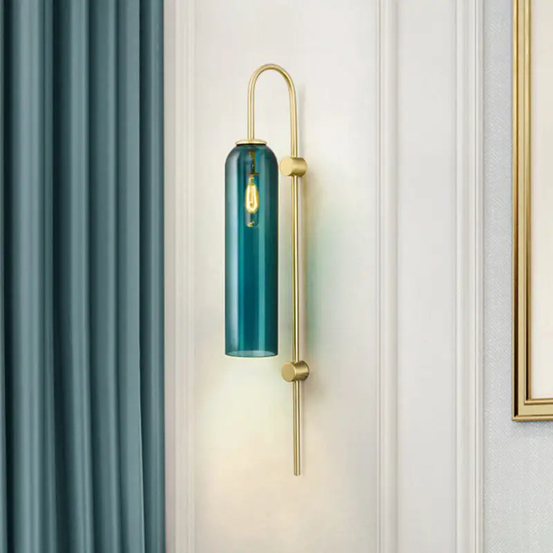 Teal cylindrical glass pendant wall sconce with a brass-finished metal frame and an exposed filament bulb.