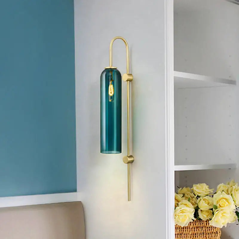 Teal glass cylinder wall lamp with gold-toned metal frame and exposed bulb for modern living rooms