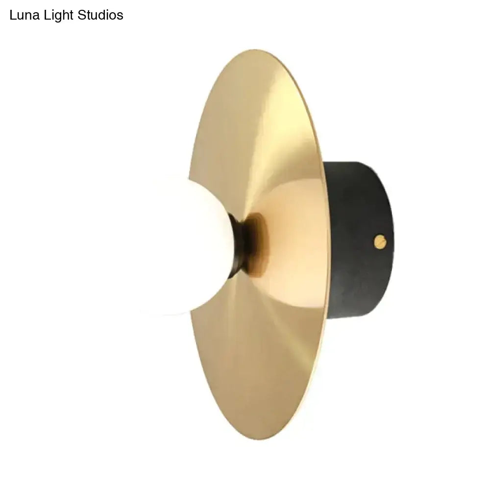 Gold-toned brass disc riya wall light with matte black cylindrical base and frosted glass bulb for bedroom use