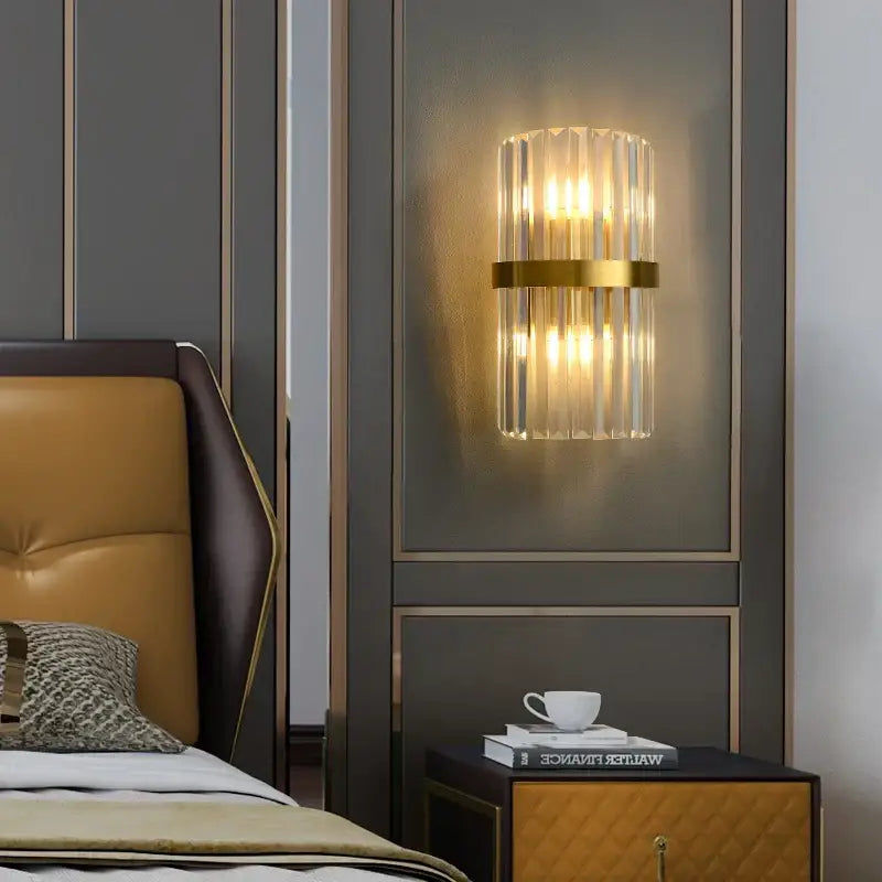 Modern gold and clear crystal led wall sconce with vertical crystal rods and gold band emitting warm light on dark wall decorbites crystal led