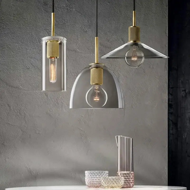 Three modern gold and clear glass led pendant lights with brass accents and geometric shades above dining table