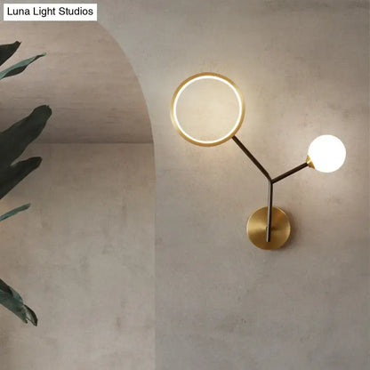 Modern gold and cream glass wall sconce lamp with brass circular ring light and spherical bulb on arched concrete wall