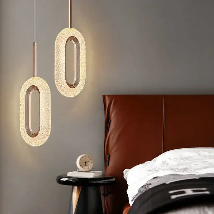 Two modern gold and crystal oval bedside pendant lights with textured warm-glowing translucent shades above bedside table