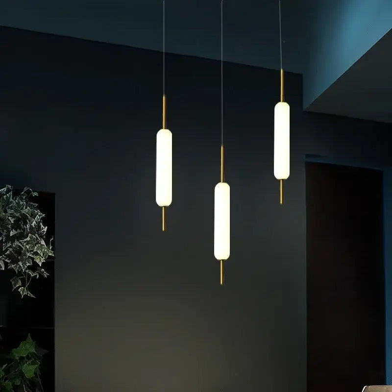Three modern gold and frosted glass led pendant chandelier lights with cylindrical shades for living room use