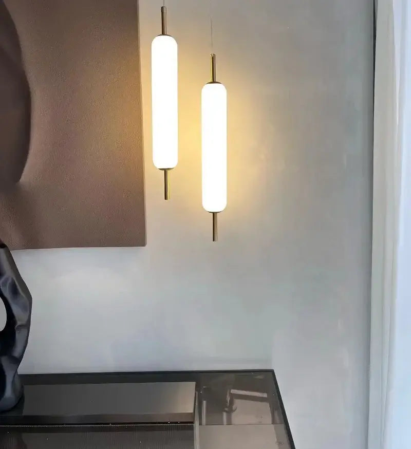 Two sleek gold cylindrical glass led pendant lights with frosted shades hanging side by side for living room