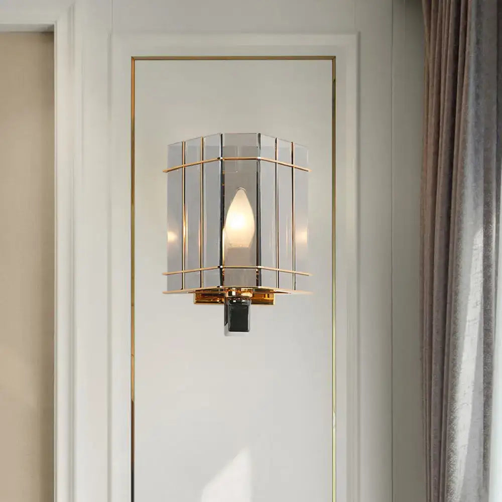 Elegant gold-framed wall sconce with gray glass triangle panels and warm glowing bulb for bedroom lighting