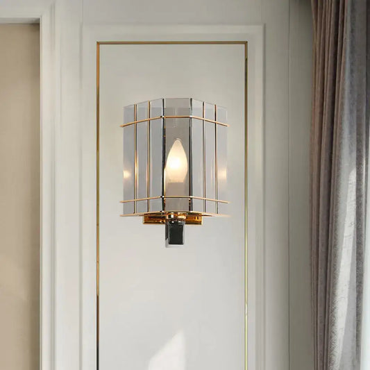 Elegant gold-framed wall sconce with gray glass triangle panels and warm glowing bulb for bedroom lighting