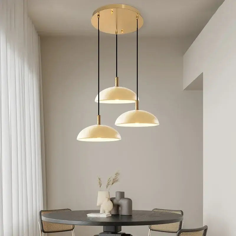 Modern pendant light with cream dome shades and gold-toned fixtures suspended by black cords for kitchen dining room