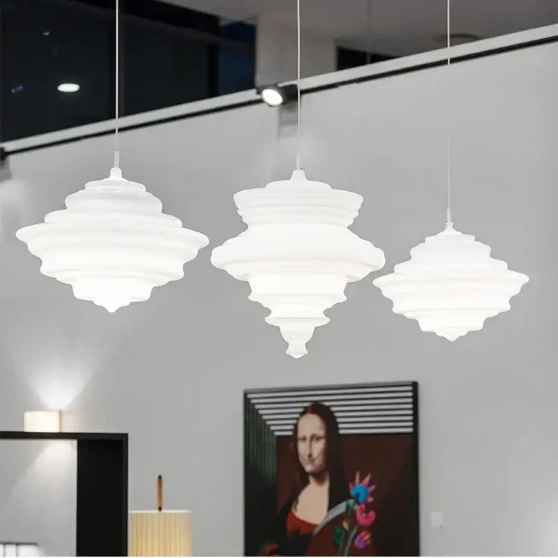 Three white tiered pendant lights with modern sculptural design in a decorbites glass chandelier for dining room