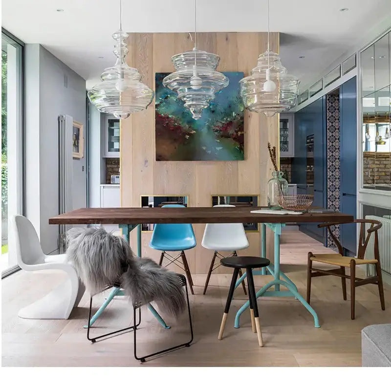 Long wooden dining table with light blue metal legs and dark brown top beneath modern decorbites glass chandelier