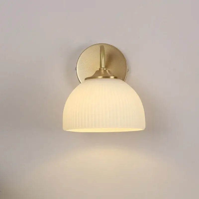 A modern gold wall lamp with warm-toned brass and a ribbed off-white white glass shade by decorbites iron white