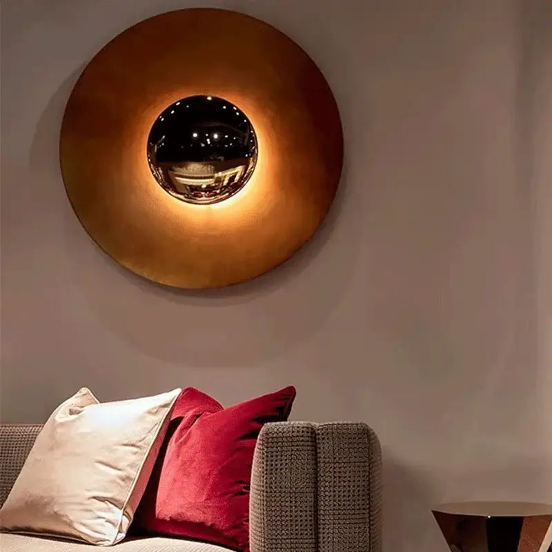 A modern led ufo wall sconce in warm brass with a central reflective chrome sphere for bedside decor