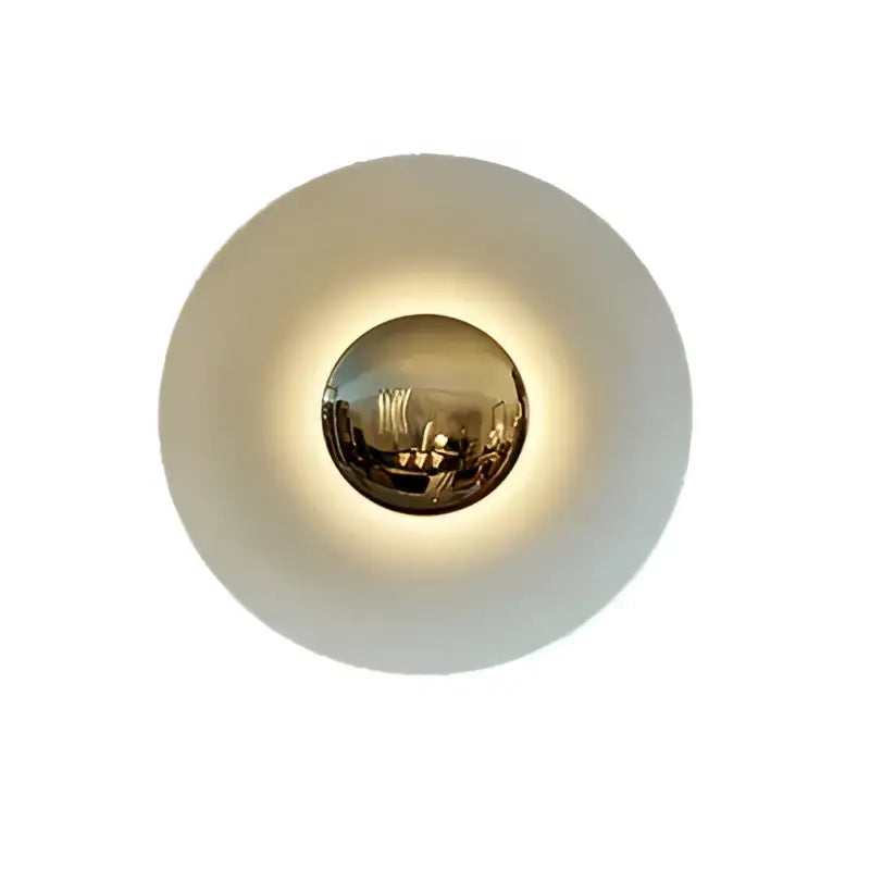 A modern gold and white led ufo wall sconce with a matte white outer ring and reflective gold sphere for bedroom ambiance
