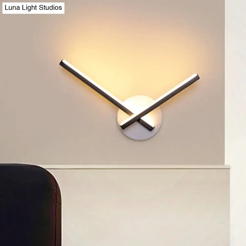 Modern gold angular wall lamp with intersecting chrome rods and circular white base emitting warm white light