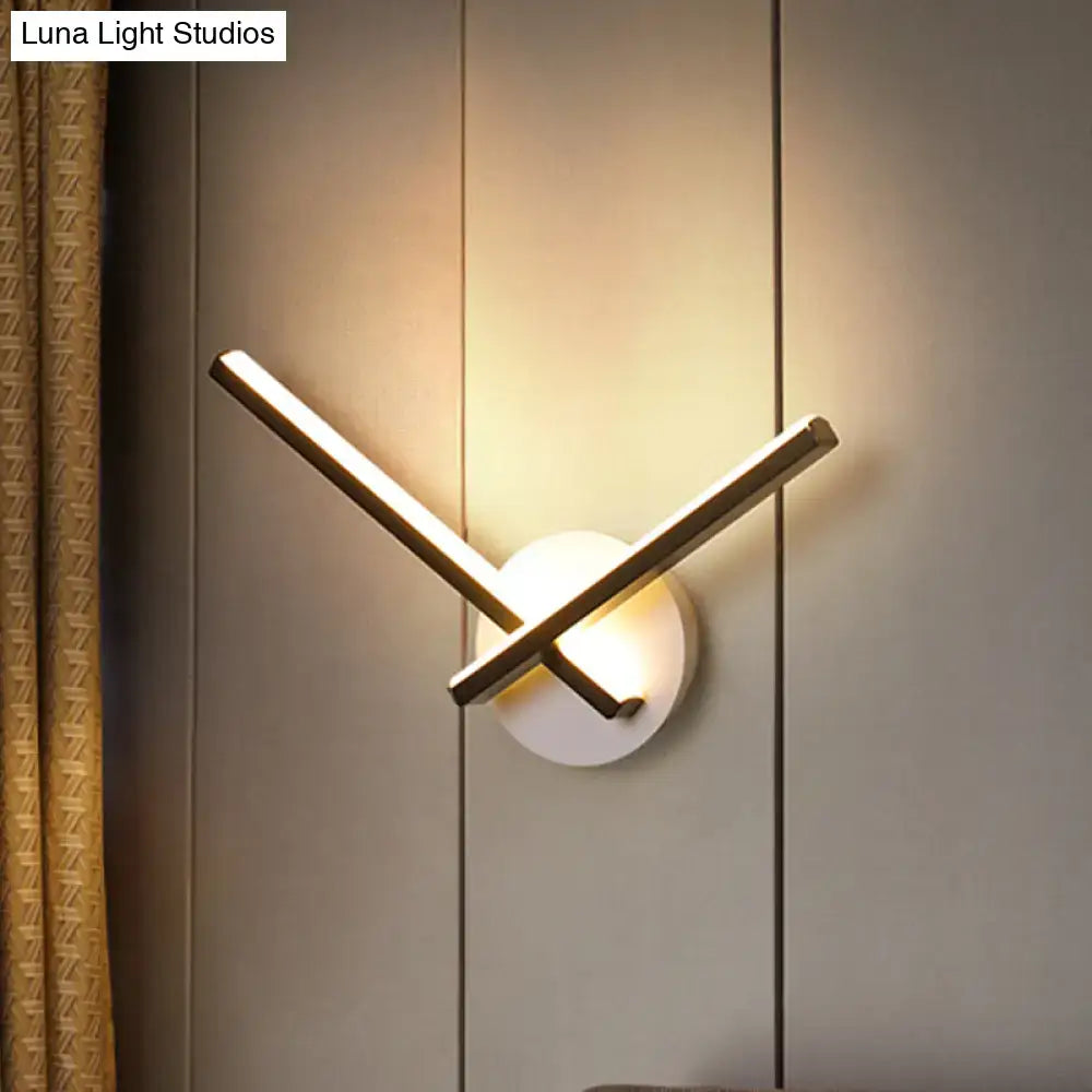 Modern gold angular wall lamp with two intersecting bars and a circular white base providing warm white light