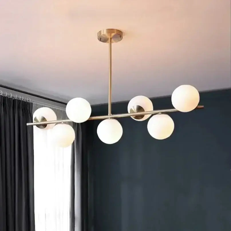 Modern gold bean glass chandelier with six frosted glass globe shades in a linear pattern for dining room lighting