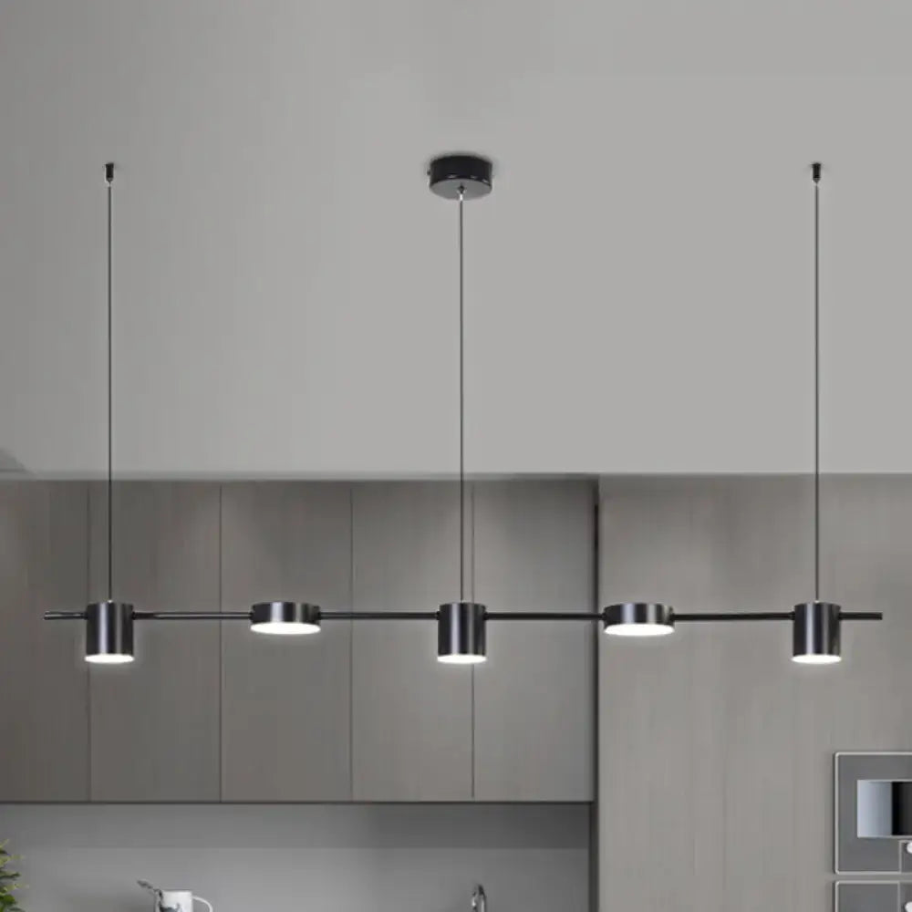 Modern black metal pendant light fixture with four cylindrical bulbs on a sleek bar emitting warm white light