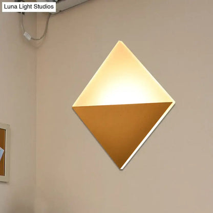 Modern gold and black wall sconce with diamond shape, warm glowing upper half, matte gold lower half, ideal for bedrooms