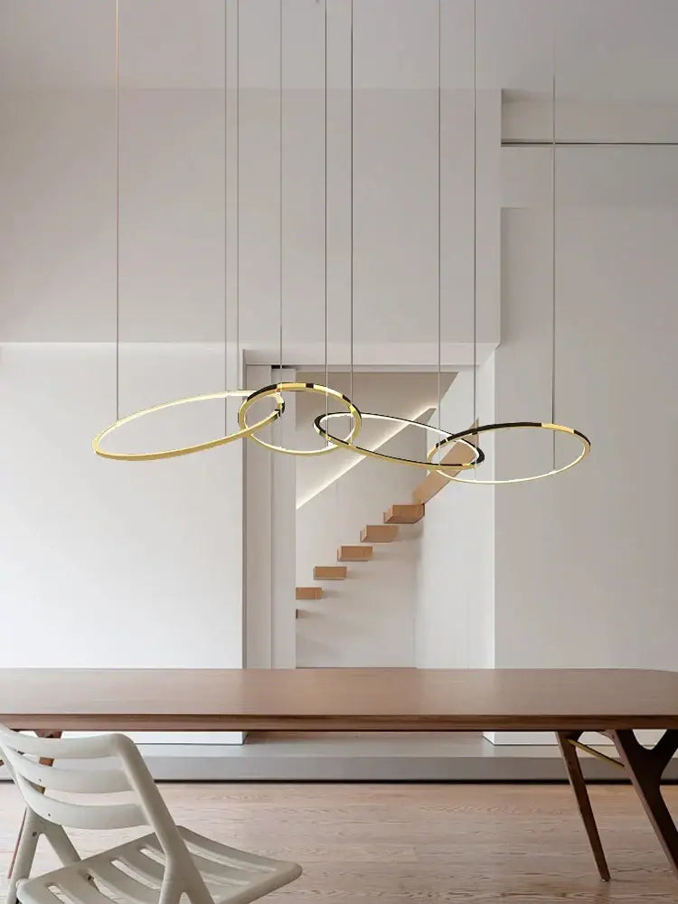 Modern gold and black stainless steel pendant lights with circular design hang above wooden dining table decorbites gold stainless