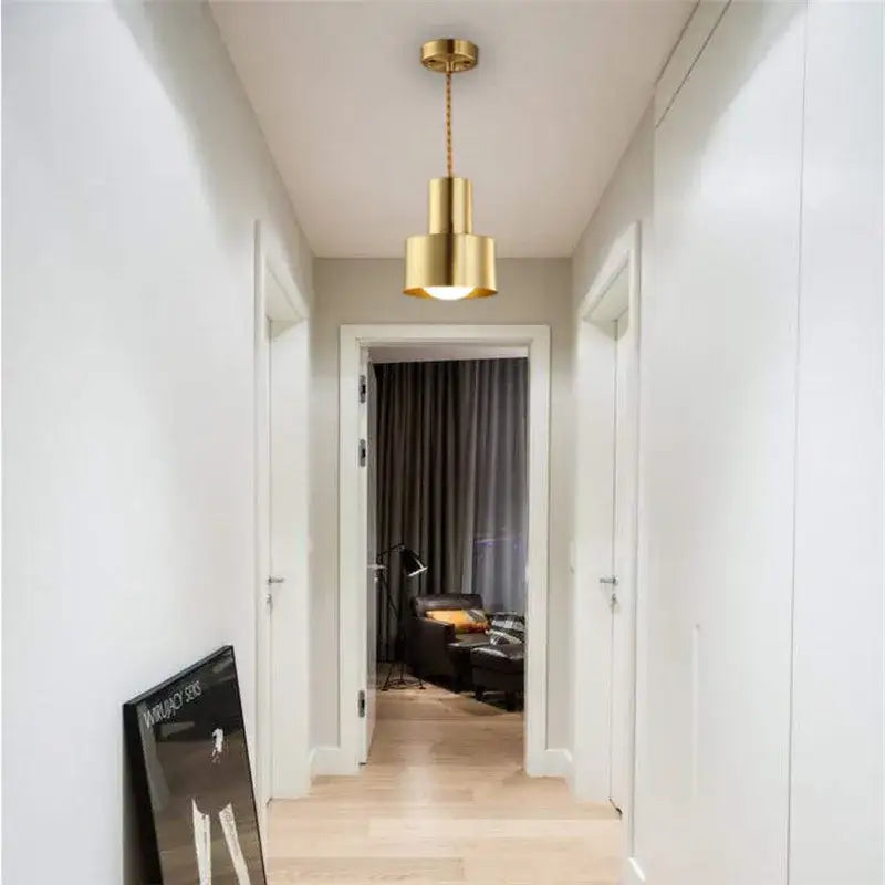 A sleek cylindrical gold brass trumpet pendant light hangs from the ceiling perfect for modern bedroom decorbites decor