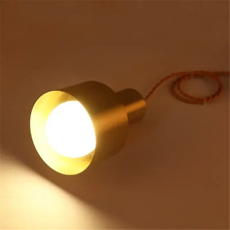 Modern gold brass trumpet pendant light with cylindrical flared design and exposed bulb emitting soft yellow glow