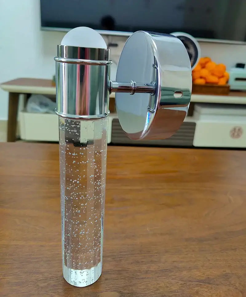 A sleek chrome wall sconce with a bubble crystal glass base filled with clear liquid for modern bedroom decorbites