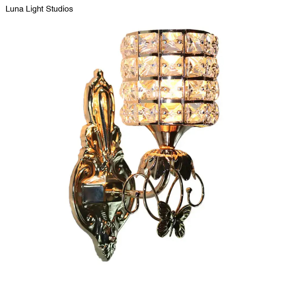 Modern gold wall light fixture with ornate design, butterfly embellishments, and cylindrical crystal shade for living room