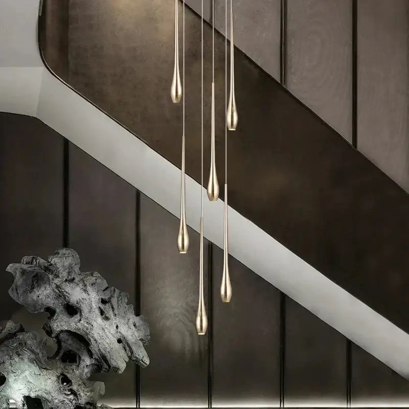 Five slender teardrop-shaped pendant lights with brushed gold finish form a modern gold cascading led ceiling chandelier