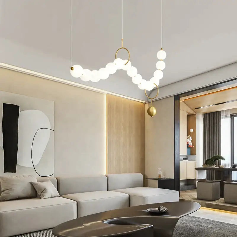 Modern gold-toned chandelier light fixture with white spherical bulbs in a curved chain design for living room use