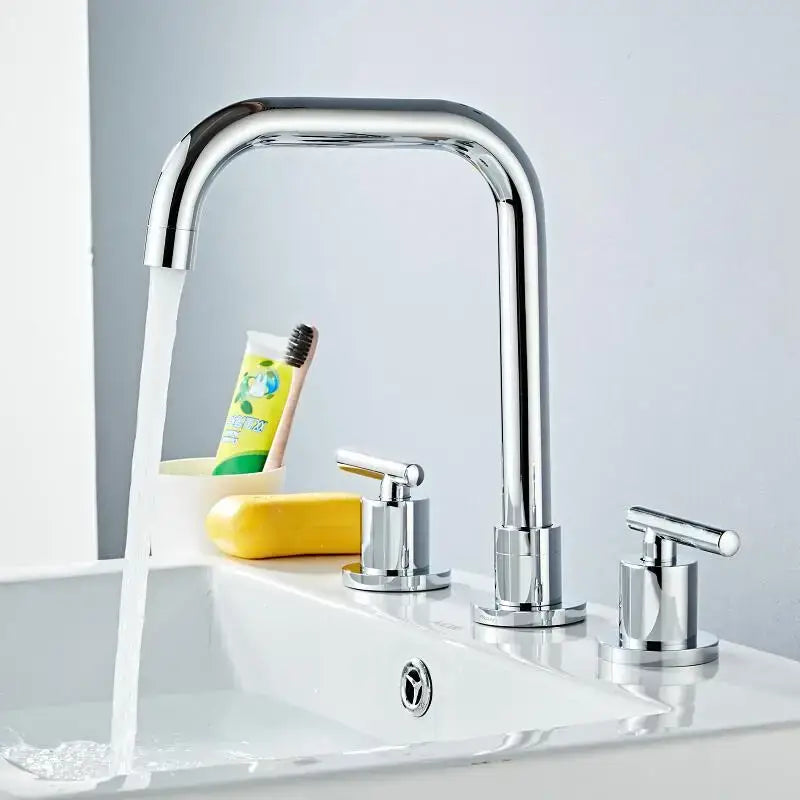 Modern gold and chrome brass basin faucet with chrome-finished sleek curved spout and three cylindrical handles for kitchen sink