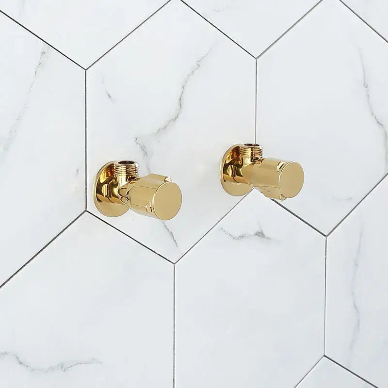 Gold-finished brass triangle valve faucet handles by decorbites mounted on white marble-patterned hexagonal tiles