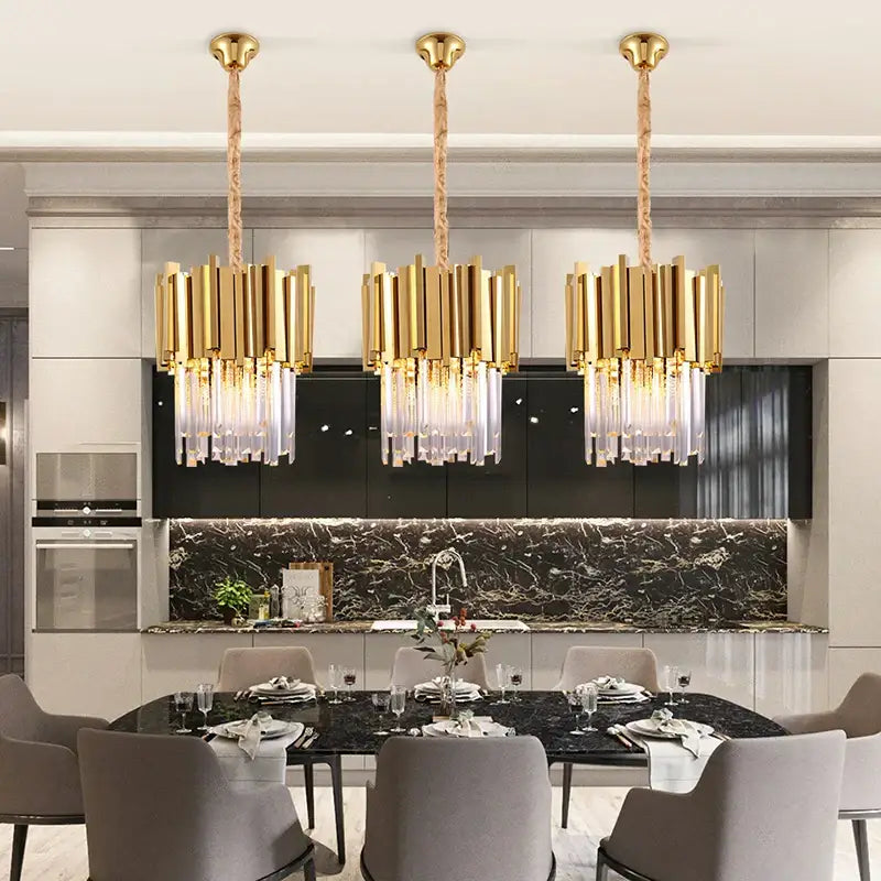 Three elegant gold and chrome decorbites crystal pendant chandeliers with cascading droplets above a dining table
