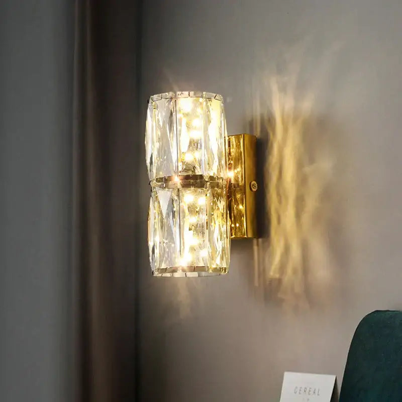 Modern gold and chrome decorbites crystal wall lamp with faceted crystal cylinders refracting warm light for bedroom decor