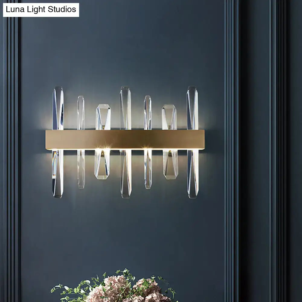 Modern gold wall sconce featuring a clear crystal bar with symmetrical prisms for elegant bedroom lighting