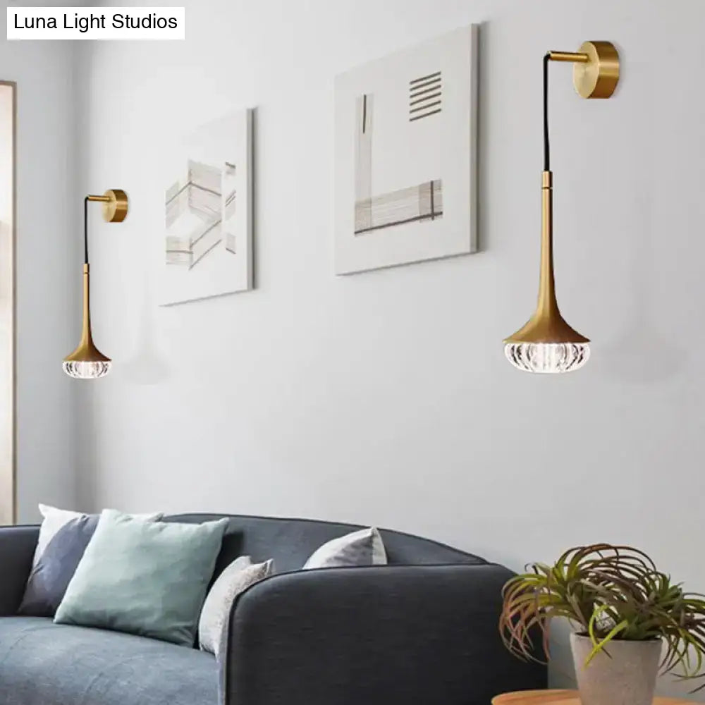 Modern gold wall sconce with a slender flared design and clear textured glass faceted shade for living room