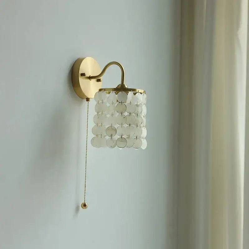 A delicate modern gold conch shell wall light fixture with translucent white shell discs and pull chain switch for bedroom