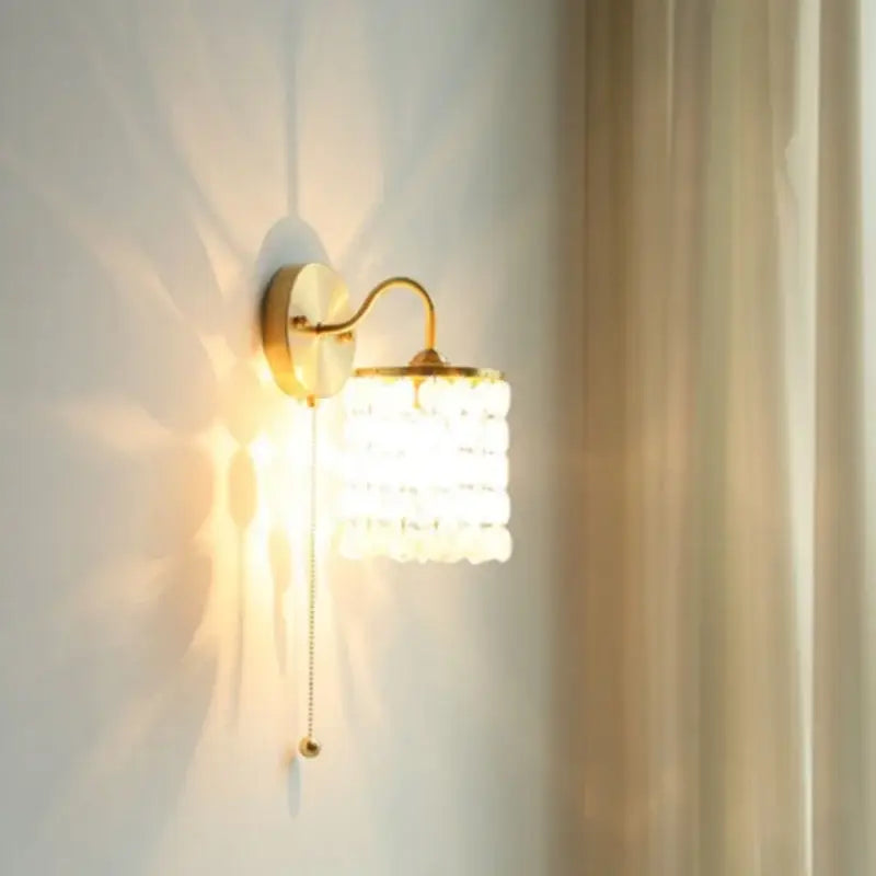 Modern gold conch shell wall light fixture with gold-toned cylindrical shade of clear faceted glass beads, pull chain switch