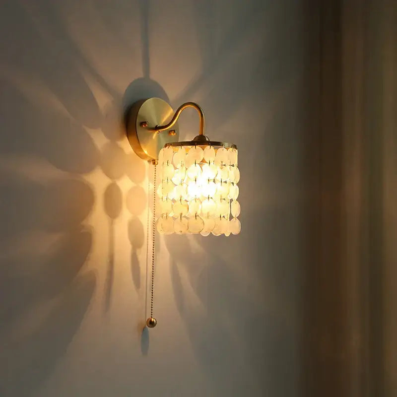 Modern gold conch shell wall light fixture with cylindrical shade of layered translucent white shell discs and pull chain switch