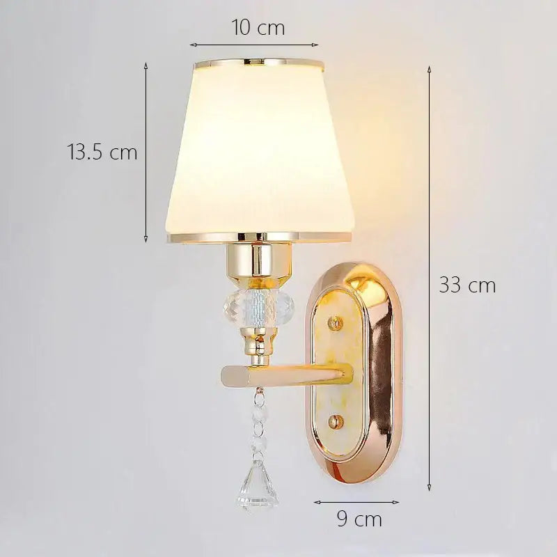 Modern gold crystal bedside wall sconce with cream fabric shade, crystal accents, and ornate gold backplate for bedroom use