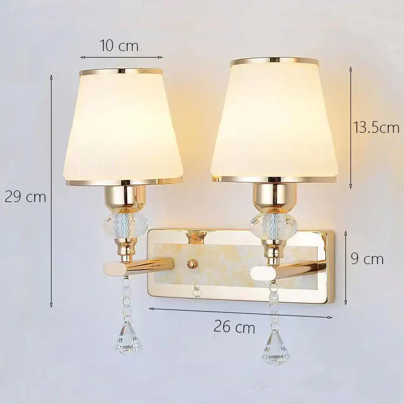 Modern gold crystal bedside wall sconce with two cream fabric shades and crystal droplets for bedroom use